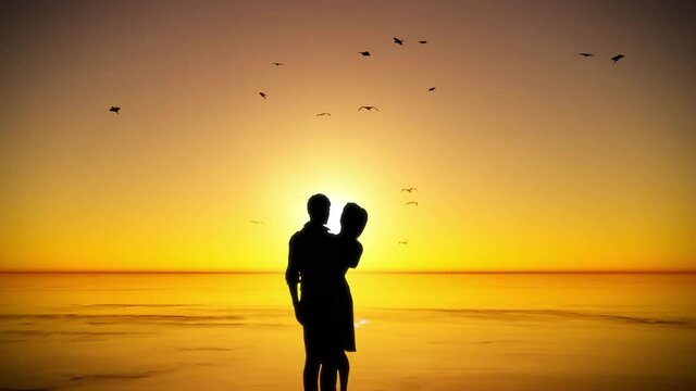 The silhouette of a couple kissing and hugging in front of a golden sunset beside the water's edge.