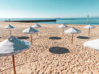 White sun umbrellas on a beach, with a view of a horizon line over the sea, sky, a symbol for...
