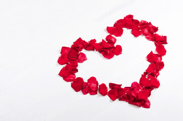 Heart of red rose petals on white wooden background