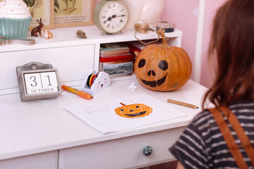 happy halloween. little girl draws a pumpkin and prepares to celebrate halloween at home