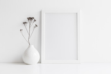 Fototapeta na wymiar Frame and dry twigs in vase on bookshelf or desk. Mockup. 