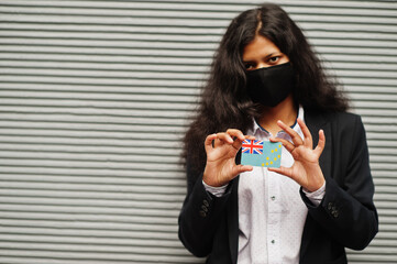 Asian woman at formal wear and black protect face mask hold Tuvalu flag at hand against gray...
