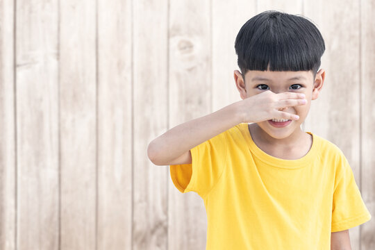 Asian little child covers nose with hand showing that something stinks with wood wall background.