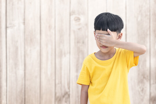 Asian little child covered his eye with wood wall background. Domestic Family violence concept. sad and unhappy child.