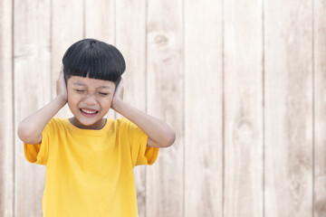 Asian little child covered his ears with wood wall background. Domestic Family violence concept. sad and unhappy child.