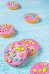 Pink glazed cookies on a blue background/surface. Dutch  cookies called Confettinis. It's a flat cake with pink fondant glazing and sprinkles.