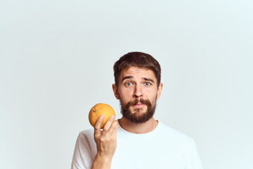 a man with an orange in a white t-shirt on a light background the diet of a brunette thick beard