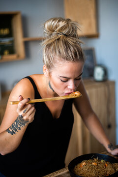 Bonita mujer joven cocinando rico. Chica rubia bonita en cocina. Mujer sonriendo a c&aacute;mara en primer plano saboreando comida.