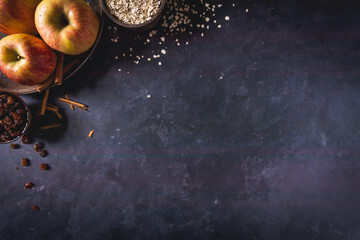 Empty dark concrete background with baking ingredients, Cinnamon, raisins, apples, oatmeal.