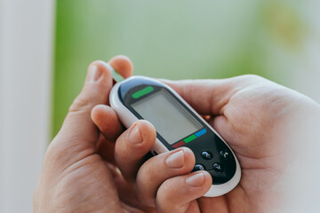 diabetes, healthcare - close up of a man with a glucometer and a test strip checking blood sugar at home