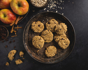 Freshly baked apple, oatmeal, raisin, cinnamon and mixed nuts cookies with ingredients on a dark concrete surface. Room for text.