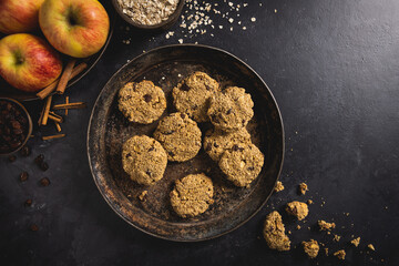 Freshly baked apple, oatmeal, raisin, cinnamon and mixed nuts cookies with ingredients on a dark concrete surface. Room for text.