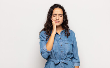 pretty young woman holding cheek and suffering painful toothache, feeling ill, miserable and...