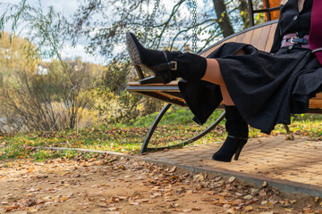 A smiling girl sits on a garden swing, forged in a burgundy coat and biret, with beautiful eyes, in the fall against the background of a pond, a blue sky.