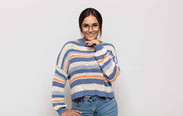 pretty young woman looking happy and smiling with hand on chin, wondering or asking a question,...