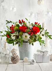Festive winter flower arrangement with red roses, white chrysanthemum and berries in vase on table...