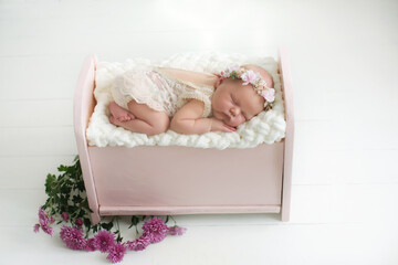 Little newborn baby girl sleeps on a pink wooden crib with a white mattress on a pink floral background, newborn photoshoot