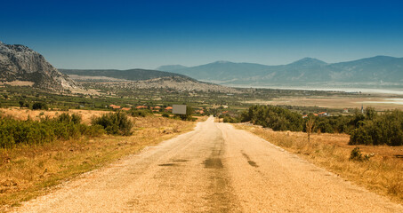 Fototapeta premium Scenic winding gravel road with a view of a lonely rocky mountain in the countryside area in Turkey. Burdur lake at the background