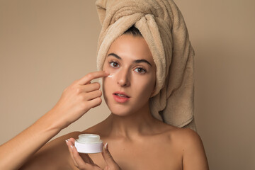 Joven Mujer mexicana con toalla en la cabeza mostrando crema facial humectante producto de belleza