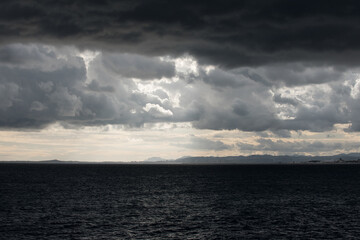 Mer et ciel nuageux très sombres et contrastés avant l'orage avec au loin vue sur la côte