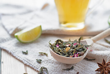 green tea leaves in a wooden spoon on linen textiles with lime slices and mug of brewed tea