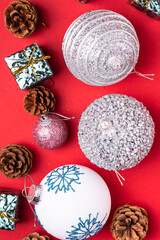Christmas New Year composition. Gifts, fir tree cones, silver ball decorations on red background. Winter holidays concept. Flat lay, top view