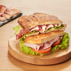 Buns stuffed with ham, tomato and salad on wooden cutting board.