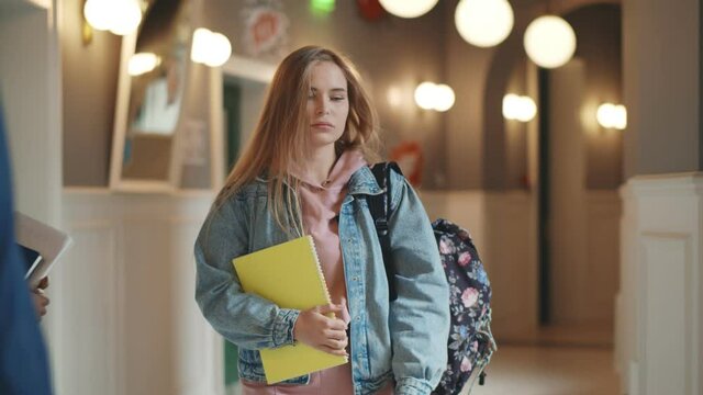 Beautiful upset woman student walking with books and backpack indoors