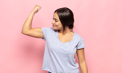 pretty young woman feeling happy, satisfied and powerful, flexing fit and muscular biceps, looking strong after the gym