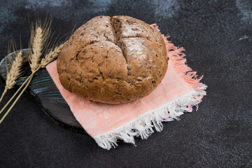 Bread with home-baked cereals on a light napkin with spikelets, dark cutting Board ,dark background. Place for a copy space