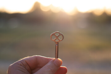 A man holds an old beautiful key in bright sunlight with his hand. Close-up with blurred background.