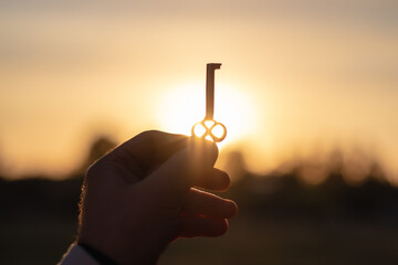 A man holds an old beautiful key in bright sunlight with his hand. Close-up with blurred background.