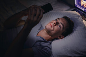 Man using mobile phone in a bed at night, blue screen before sleep