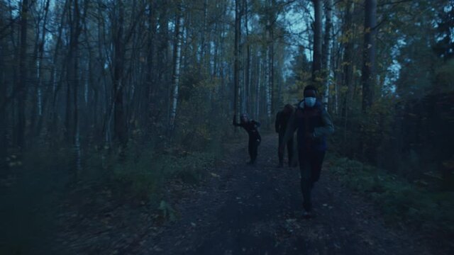 Zombie couple chasing african man in safety mask in twilight woods