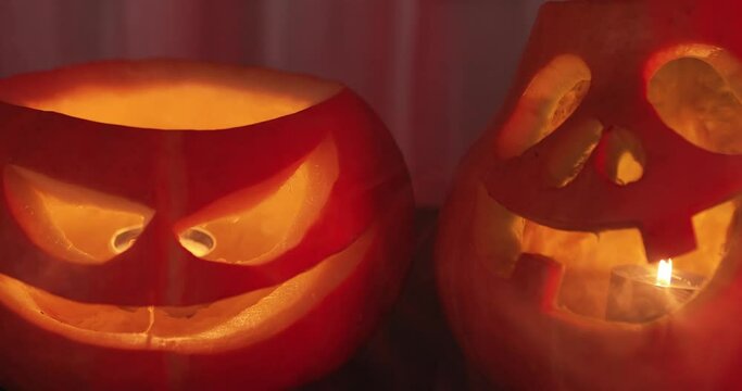 Two spooky pumpkins glowing inside jack lantern face with smoke at dark background and police or ambulance blue red light. Traditional orange carved pumpkin symbol in fog. Halloween night home party.