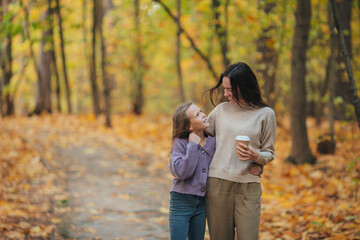 Little girl with mom outdoors in park at autumn day