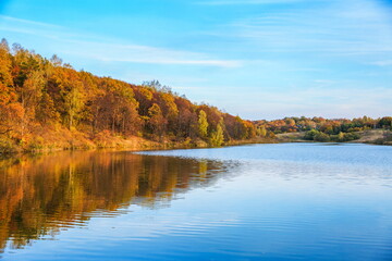 Fototapeta na wymiar autumn landscape of lake and orange forest on the slope. panoramic view of the forest river on a sunny autumn day