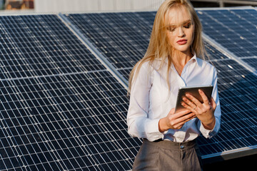 Investor woman stand with tablet near blue solar panels row on the ground Girl weared formal white shirt. Free electricity for home. Sustainability of planet. Green energy.