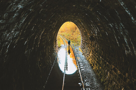 Dark flooded single track tunnel with a standing man. Urbexer in old abandoned railway tunnel.