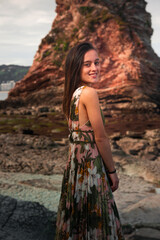 Fototapeta na wymiar Young girl with a colorful dress posing at a rocky cove at the basque coast.