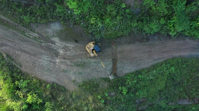 High angle view of an excavator that is working on the road and removing some bushes 
