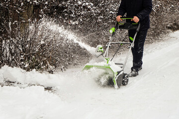 Man cleans snow off path with wireless electric snow blower