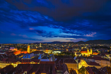 Naklejka premium City lights of Graz and Mariahilfer church, view from the Schlossberg hill, in Graz, Styria region, Austria, after sunset. Dramatic sky, panoramic view.