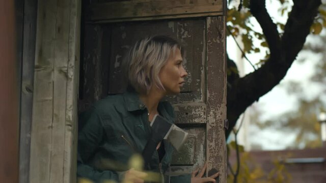 Woman with axe walking out of shack and running away during zombie apocalypse