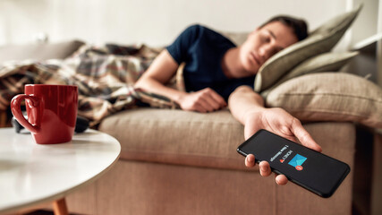 Teenage guy falling asleep with smartphone holding in hand, lying on the couch at home. New message from his girlfriend on the screen. The concept of smartphone addiction