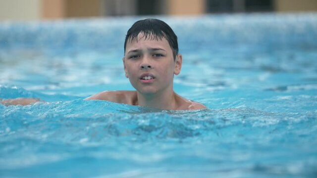 Smart boy playing and splashing water with his hand in a swimming pool in slo-mo 