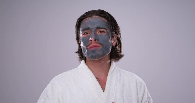 Handsome man in bathrobe with anti aging clay face mask