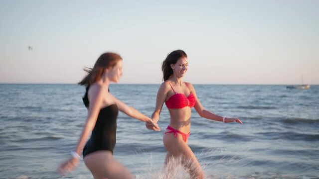 happy summer, cheerful female friends have fun enjoying on coast running holding hands background of sea and splashes during holidays