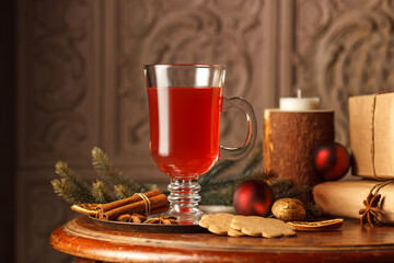 The concept of the winter holidays. Mulled wine in a glass glass, on a copper tray with spices, fir branches. On a vintage wooden table with gifts. Close-up, low key