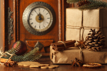 Gifts close-up in craft paper with winter spices and fir branches. Vintage clock on the mantelpiece...